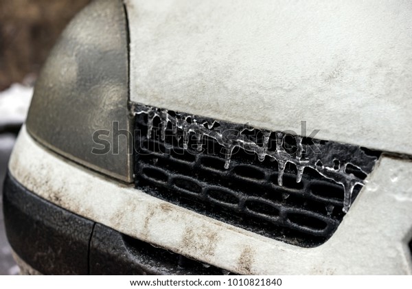 Car coated ice crust during the \
icy rain in cold weather. Front part of the car\
headlights