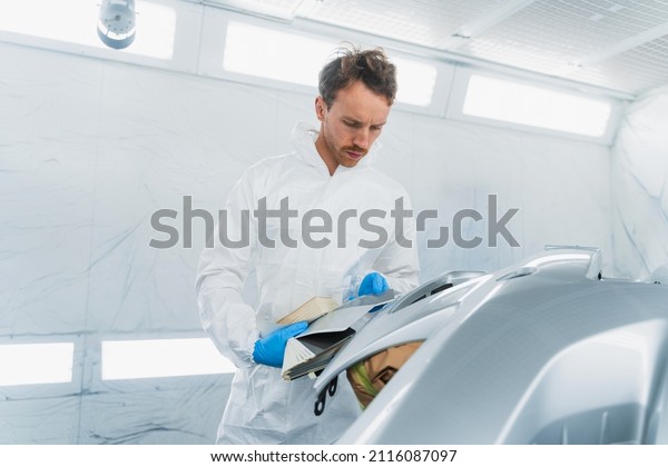 Car colorist man selecting color of\
automobile body element with paint matching\
samples