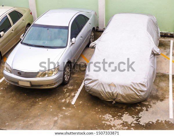 Car cover. Close up\
of a car parked with a protective cover white sheet for sunlight\
and rain protected on hot and wet weather in the parking lot. -\
High Resolution image.