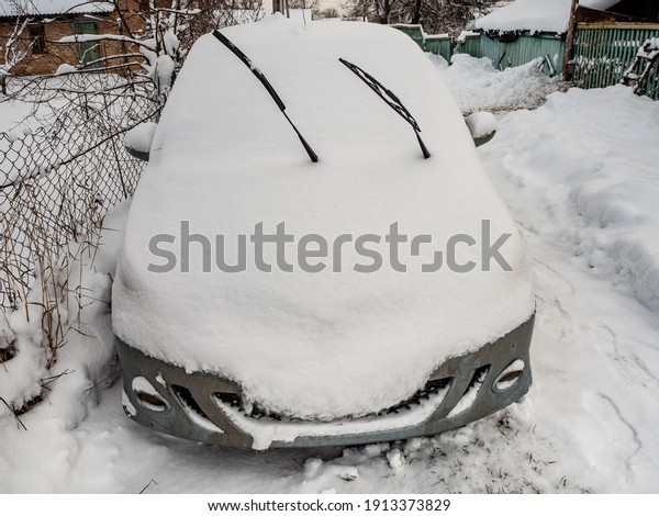 Car covered with snow in the countryside, after a\
snowfall, front view