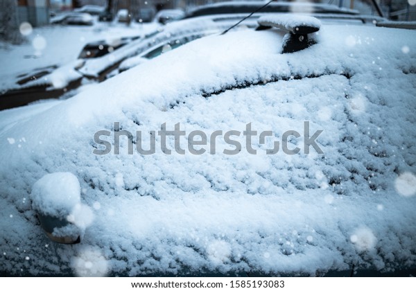 The car is covered in snow.\
In the frame, the side. Snow falls. Glass in focus blurred\
background.