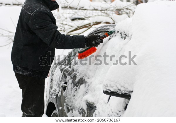 A car covered with snow. A man cleans the car\
from snow with special\
brushes.