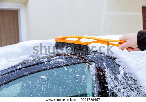 A car covered with snow. A man\
cleans the car from the snow with his hand with special\
brushes.