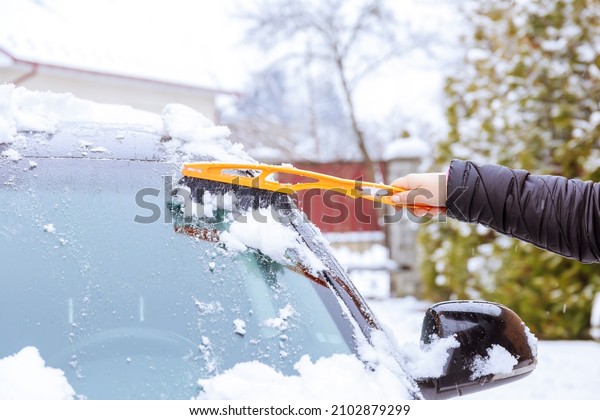 A car covered with snow. A man with his hand
cleans the windshield of the car from the snow with special
brushes. Frosty weather.