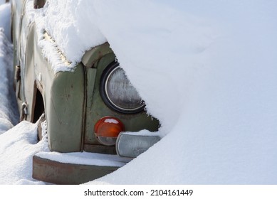 Car Covered With Snow. One Headlight Is Visible.