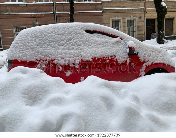 The car was covered with snow in the parking lot.\
Cars under a large layer of snow. Snowfall on the streets of a\
European city.