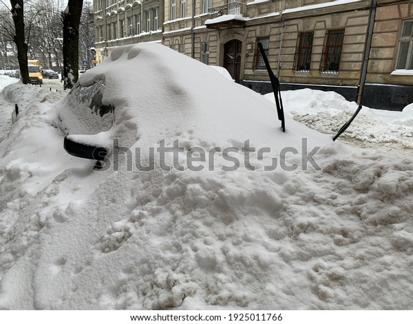 The car was covered with snow in the parking lot.
Cars under a large layer of snow. Snowfall on the streets of a
European city.