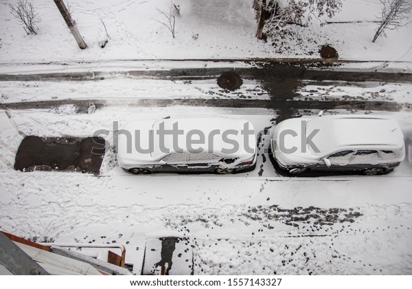 The car, covered with thick layer\
of snow. Negative consequence of heavy snowfalls. parked cars\
covered with snow during snowing in winter time. Top\
view.