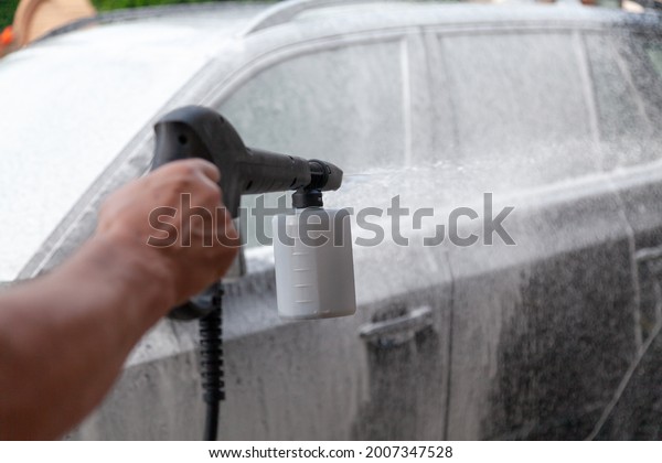 car is covered with white\
foam. Hand sprays detergent with a plastic high pressure washer\
gun\
\
