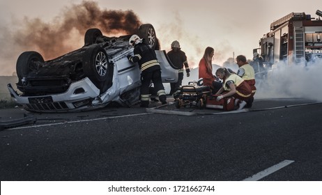 Car Crash Traffic Accident: Paramedics and Firefighters Rescue Injured Trapped Victims. Medics give First Aid to a Female Passenger. Firemen Use Hydraulic Cutters Spreader to Open Vehicle