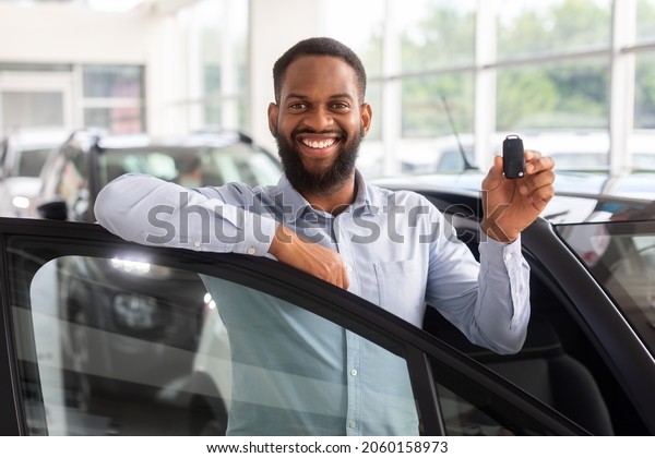 Car Credit Concept. Happy Black Male With Car Keys\
In hand Posing Near New Automobile, Cheerful African American Man\
Leaning On Automobile Door And Smiling At Camera, Closeup Shot With\
Free Space