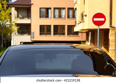 Car with dark tinted windows in an urban street below colorful apartment blocks and a no entry sign, close up view of the windshield