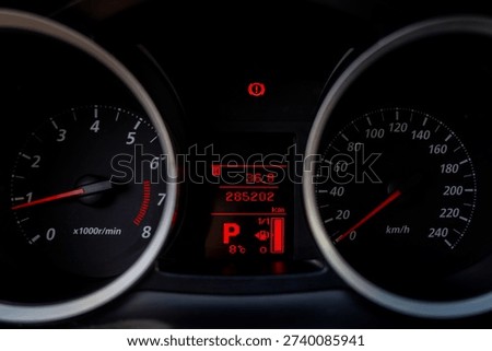 Car dashboard with speedometer and tachometer, central digital display showing odometer reading, gear position and temperature indicator.