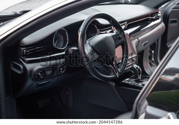 Car dashboard and steering wheel with media control\
buttons. Black cockpit. Luxury vehicle interior. Background on the\
theme of cars