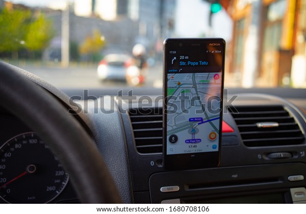 In car\
dashboard view with smartphone showing Waze maps to show the way\
thru the city in Bucharest, Romania,\
2020