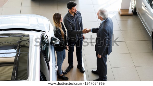 Car dealer\
giving a handshake to a young\
couple