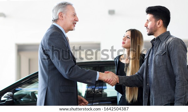 Car dealer\
giving a handshake to a young\
couple