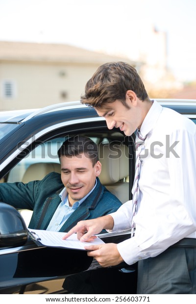 Car dealer and happy smiling man signing a\
contract. Concept for car rental\
