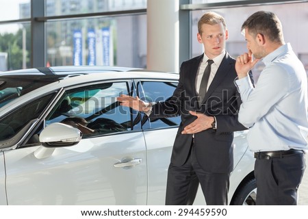Car dealer showing vehicle to mature man