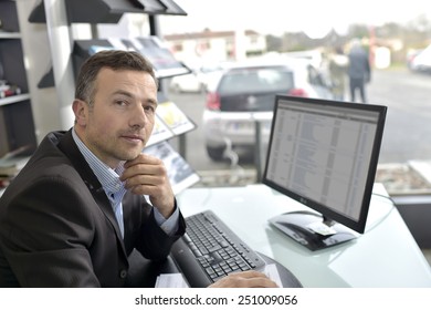 Car Dealer Sitting In Front Of Desktop Computer