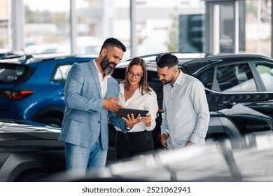 A car dealer utilizes a tablet to enhance a couple's understanding and engagement in the car purchasing process, emphasizing modern techniques in an inviting showroom setting. - Powered by Shutterstock