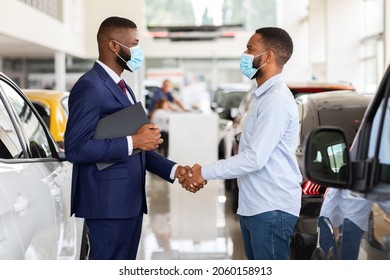 Car Dealership. Black Salesperson In Medical Mask Car Sales. Shaking Hands With Male Customer In Modern Showroom, Happy African American Man Buying New Automobile During Coronavirus Pandemic