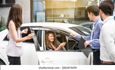 Car Dealership. The Caucasian Woman Client In The New Car Is Receiving The Car Key From The Sales Team Before Hand Over. Auto Leasing Business.