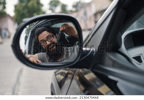 Car dealership, the happiest\
client. Charismatic man holding car keys smiling, with teeth, while\
sitting in the car looking to himself in the side mirror\
reflection.