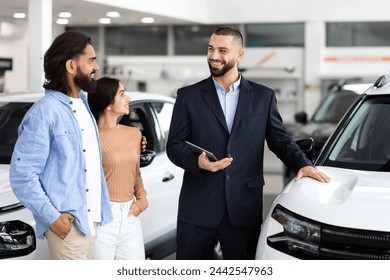 A car dealership interaction where a salesman smiles while discussing with indian couple beside a vehicle - Powered by Shutterstock