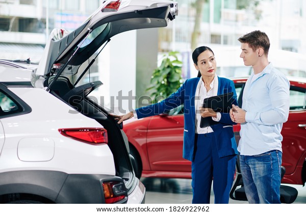 Car dealership manager opening car trunk when\
showing automobile to\
customer