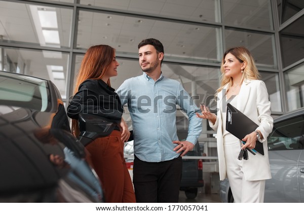 Car dealership manager shows cars to a young\
family couple