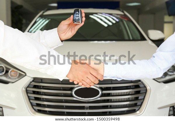 Car dealership sales person at work concept.\
Portrait of young sales representative wearing formal wear suit,\
showing vehicles at automobile exhibit center. Close up, copy\
space, background.