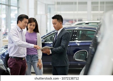 Car Dealership Salesman Showing Information On Tablet Computer To Customers