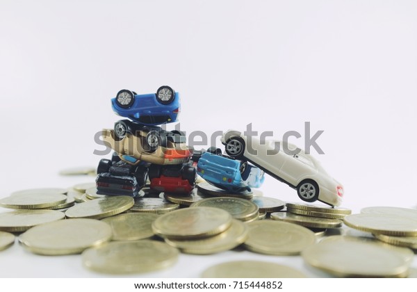 Car debt and money\
problem concept, white miniature car on toy car overturn downside\
and overlapping another on pile of gold coins money in low light\
white background 