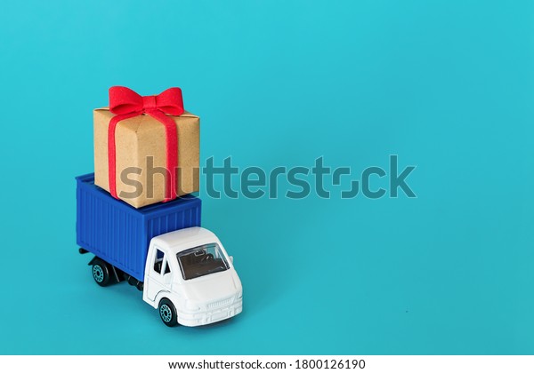 Car delivering\
gift box on blue background. Cargo transportation, delivery\
service. Transport company. Infrastructure and logistics. Unloading\
cardboard box. Place for\
text