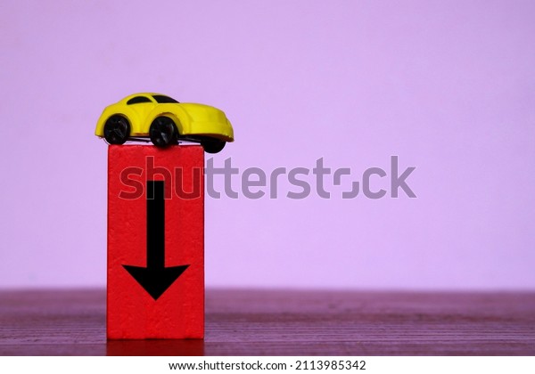 Car depreciation value, price\
drop concept. Toy car and red wooden cubes with downward\
arrow.