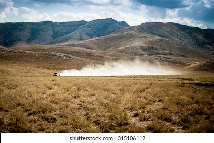 A car in the desert quickly rides through the mud with clouds of dust from under the wheels, against the backdrop of the mountains. Dakar Rally. SUV rides off the road