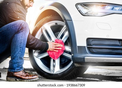 Car detailing close up. Man holds red microfiber in hand and polishes the wheel alloy tire. Selective focus. Car detail washing or cleaning.