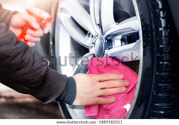 Car detailing close up. Man holds red\
microfiber in hand and polishes the wheel alloy tire. Selective\
focus. Car detail washing or\
cleaning.