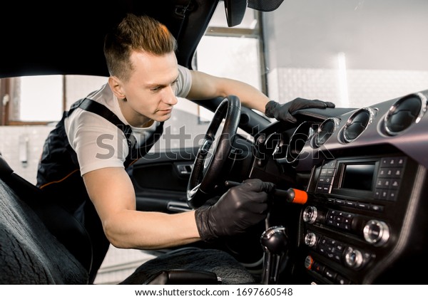 Car detailing concept.\
Brush cleaning off dust from the car interior details, control\
panel. Young Caucasian man cleaning car interior with brush.\
Selected focus on hand