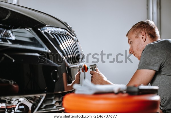 Car detailing, concept of details and polishing\
cars. hands of a professional car service male worker with orbital\
polisher polishing a white luxury car hood in a car repair\
shop