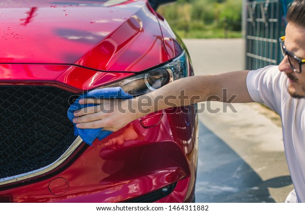 Car detailing - the man holds the microfiber in\
hand and polishes the car. Selective focus. Car detailing series :\
Worker cleaning red car. 