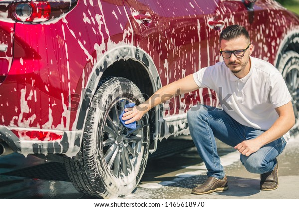 Car detailing - the man holds the microfiber in\
hand and polishes the car. Selective focus. Car detailing series :\
Worker cleaning red car. 