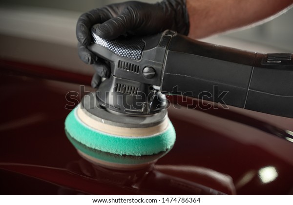 Car detailing man with orbital polisher in auto repair\
shop. close up