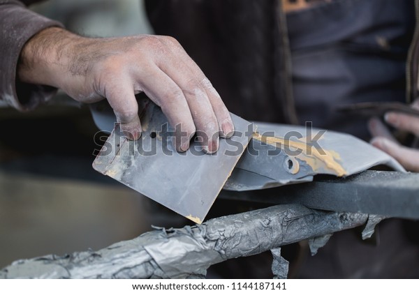 Car detailing - Man with sandpaper in auto\
repair shop sanding polishing and preparing car parts for painting.\
Selective focus on man\'s\
hand.