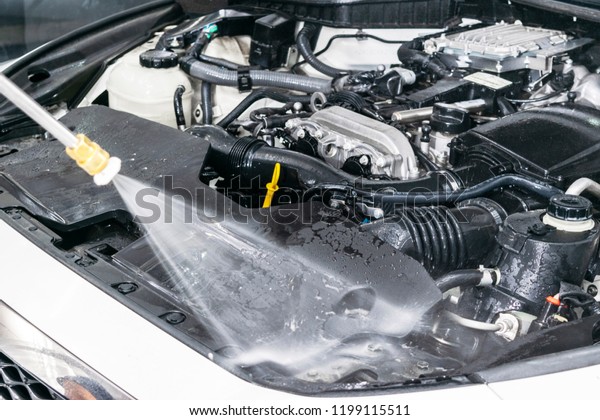 Car detailing. Manual car\
wash engine with pressure water. Washing car engine with water\
nozzle. Car cleaning concept. Man spraying pressure water for\
engine wash