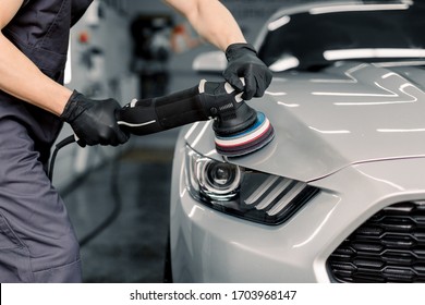 Car detailing and polishing concept. Hands of professional car service male worker, with orbital polisher, polishing white luxury car hood in auto repair shop