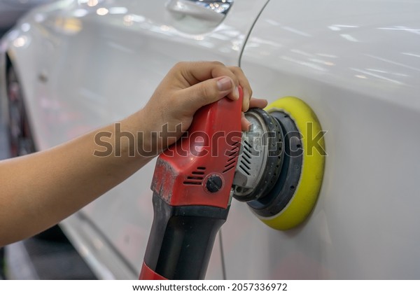 Car detailing and polishing concept.\
Hands of professional car service male worker with orbital\
polisher, polishing luxury car hood in auto repair\
shop