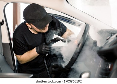 Car Detailing, Steam Cleaning Concept. Handsome Man In Black T-shirt And Cap, Worker Of Car Wash Center, Cleaning Car Interior With Hot Steam Cleaner. Car Detailing Concept