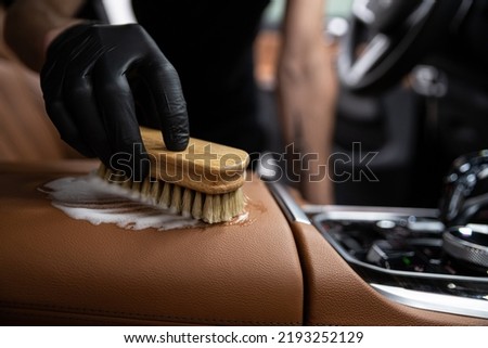 car detailing studio employee cleans the brown leather upholstery of a car 